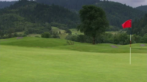 Hilly golf course with red flag fluttering at right of frame; rural landscape in Stock Footage 59536544