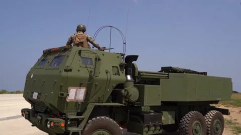 HIMARS being driven across dirt runway with C-130 Hercules in background Vídeos de archivo 150800238
