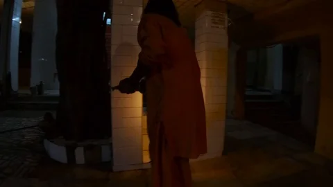 Hindu monk performs evening aarti with light fixture near banyan tree Stock Footage 100334077