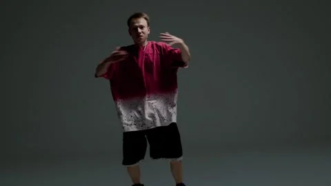 Hip hop dancer crouching with arms extended in a dark studio Stock Footage 345601665
