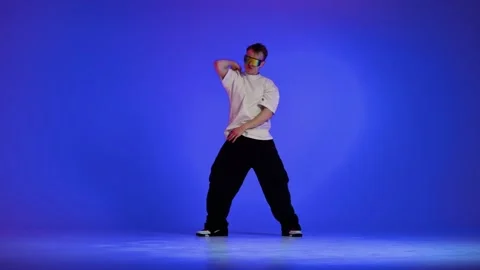 Hip hop dancer performing rhythmic freestyle on blue studio background Stock Footage 345602161