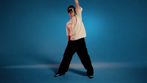 Hip hop dancer performs dynamic freestyle move against blue studio background Stock Footage 345602113