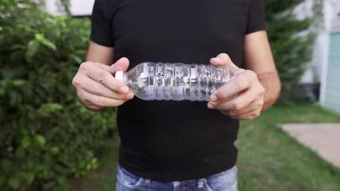 Hip level shot of a man crumbling a plastic bottle at her backyard garden Stock Footage 139872618