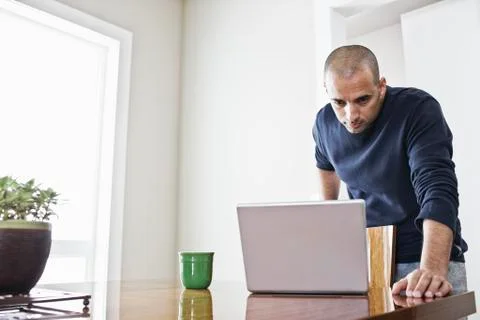 Hipanic man checking his laptop computer at the dinning room table in a new Fotos de archivo