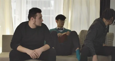 Hippie boy and plump guy talking and watching TV as their nerd Caucasian friend Video stock 123561960