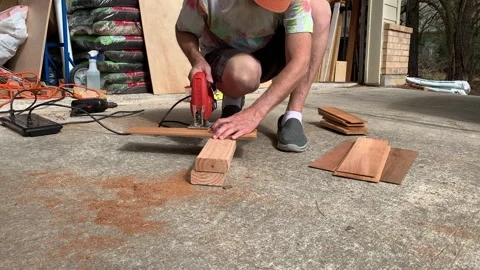 Hippie man with beard cutting cedar shingles with jigsaw for tiny house Stock Footage 146756197