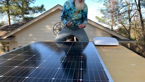 Hippie man installing solar panel on roof of tiny house/van conversion Stock Footage 146756214