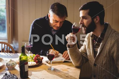Hipster and mature man tasting red wine and taking notes in country house Stock Photos