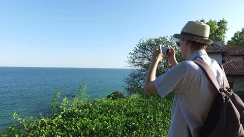 Hipster with backpack taking photos of the seaside with his phone in summer day Stock Footage 71965730