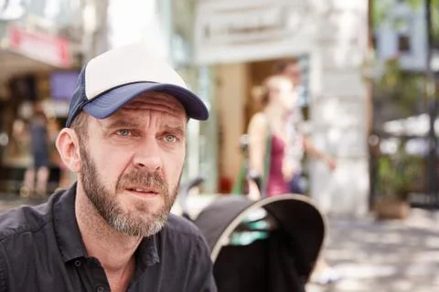 Hipster with beard and baseball cap sitting in a street cafe Stock Photos