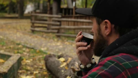 A hipster with a beard and a cap drinks pu-erh tea from a bowl. outdoor Stock Footage 220415422
