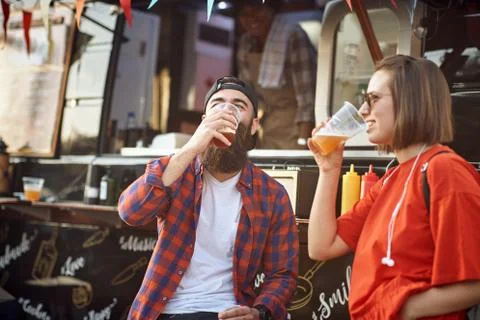 Hipster couple drinking beer in front of food truck; Urban lifestyle concept Stock Photos