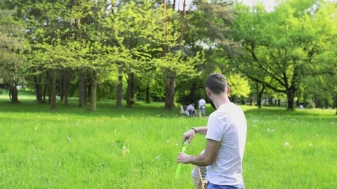 Hipster father and son blowing bubbles outdoors in park. Stock Footage