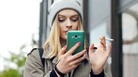 Hipster girl smoking cigarette and browsing internet on smartphone