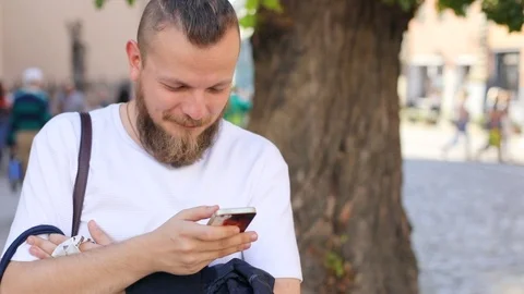 Hipster guy with a beard with a smartphone in his hand in a T-shirt camera moves Video stock 100731571