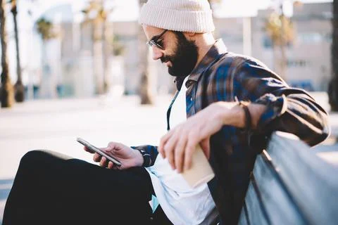 Hipster guy with coffee to go browsing wireless on smartphone Stock Photos