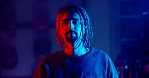 Hipster guy with dreadlocks looking at camera while smoking a hookah in neaon Vidéo 131882545