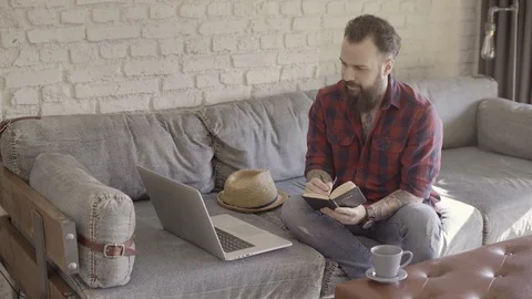 Hipster guy is taking some notes from his laptop Stock Footage 72530475