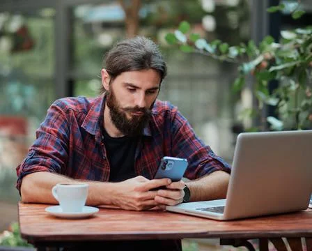 Hipster guy using his smart phone in a cafe while studying. Stock Photos