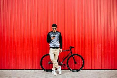 Hipster guy using a smartphone, standing near the bike, outdoors. Stock Photos