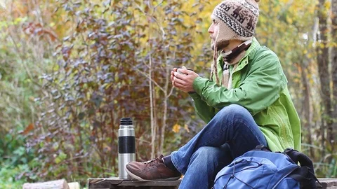 Hipster man sits, warms hands and drinks tea or coffee, dreams and smile, autumn Video stock 103122633