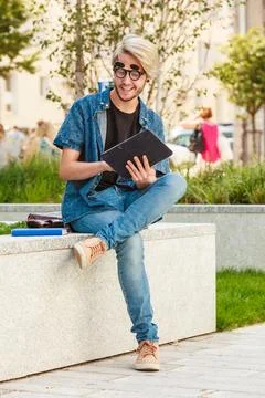 Hipster smiling guy with tablet sitting on ledge Stock Photos
