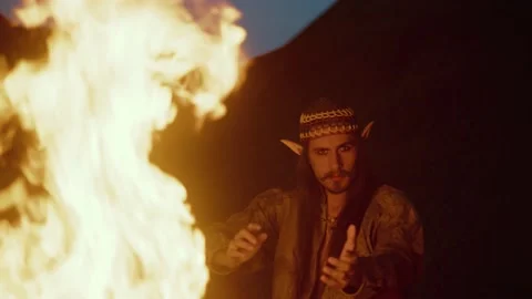 Hipster young man siting by the bright bonfire and looking at the camera . Stock Footage 239152140