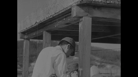 Hiroshima 1940s: A man wearing a cap and glasses stands beside a wooden Stock Footage 340926853