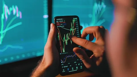 His focused hands typing away on a smartphone screen amidst a sea of charts and Stock Footage 232892719