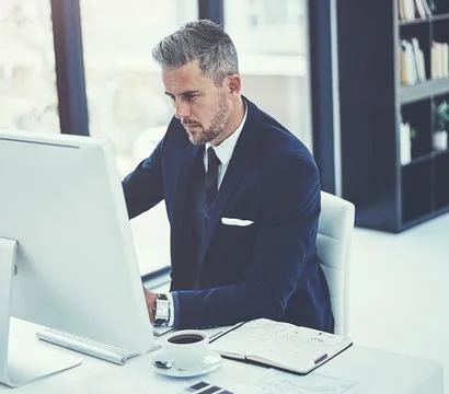 His hard work got him here. a mature businessman using a computer at his desk in 스톡 사진