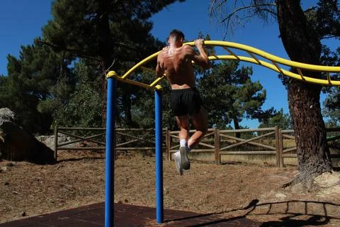 Hispanic athletic topless man doing a pull-up on parallel bars on a sunny day. Stock Photos