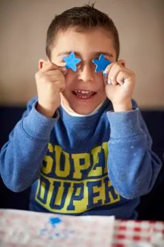 Hispanic boy covering eyes with blue stars at table Stock Photos