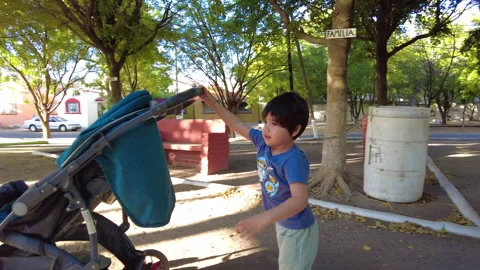 Hispanic boy playing in a playground with a stroller 動画素材 263873214