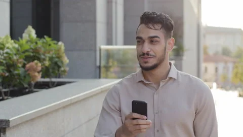 Hispanic business man smiling walking city street looking at mobile phone online Stock Footage 161419853