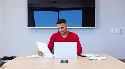 Hispanic businessman analyzing document while sitting with laptop at conference Stock-Fotos