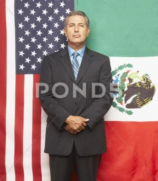 Hispanic businessman in front of American and Mexican flags Stock Photos