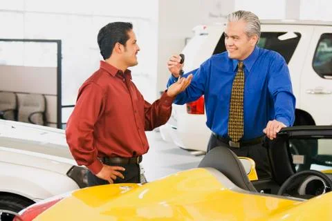Hispanic car salesman handing car keys to buyer Stock Photos