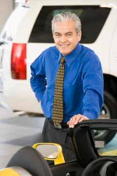 Hispanic car salesman leaning on new car Stock Photos