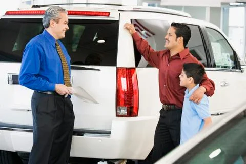 Hispanic car salesman talking to father and son Stock Photos