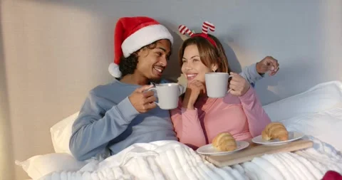 Hispanic couple seeing breakfast tray wearing Santa hat and antlers clinking Stock Footage 344225766