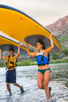 Hispanic couples carrying paddle boards in water Stock Photos