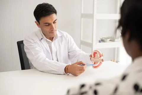 Hispanic dentist explaining to patient about teeth and how to brush with de.. Stock Photos