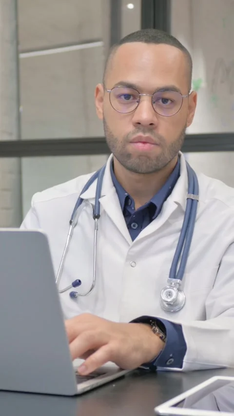 Hispanic Doctor Looking at Camera while Working on Laptop, vertical video Video stock 325700988