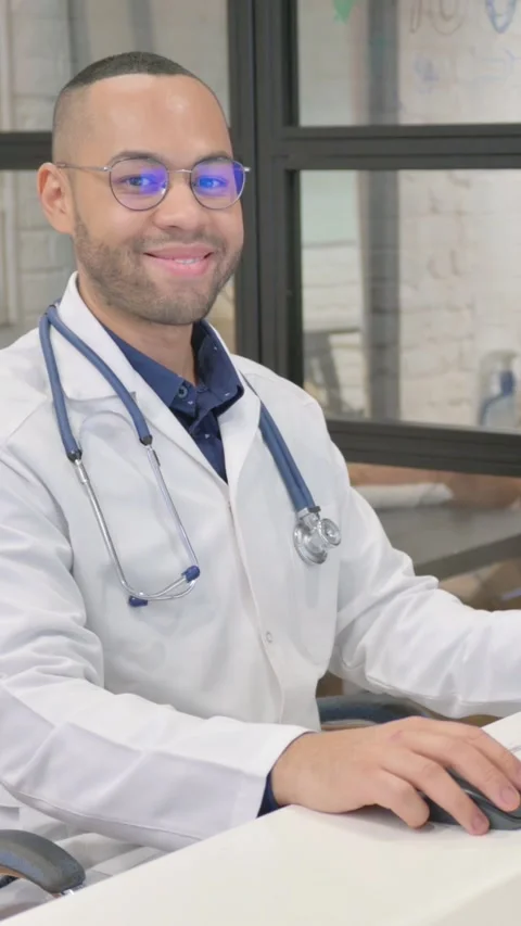 Hispanic Doctor Smiling at Camera while Working on Desktop, vertical video Video stock 325701147