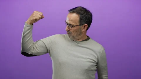 Hispanic elderly man flexing arm on isolated purple background wearing glas.. Stock Footage 311527189