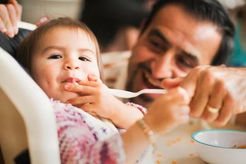 Hispanic father feeding daughter in high chair Stock Photos