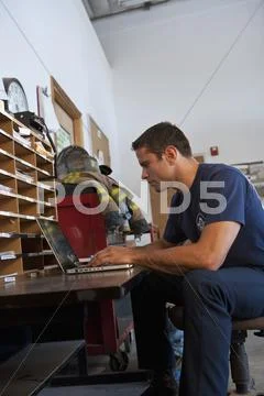 Hispanic Fireman Using Laptop In Office