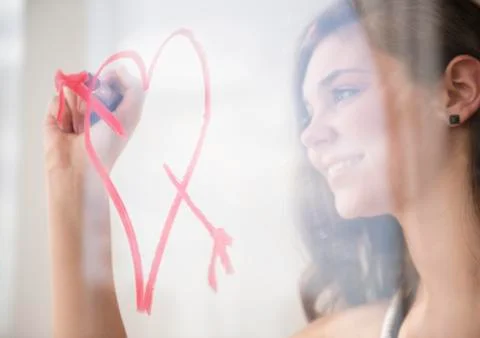 Hispanic girl drawing heart with arrow on window Stock Photos