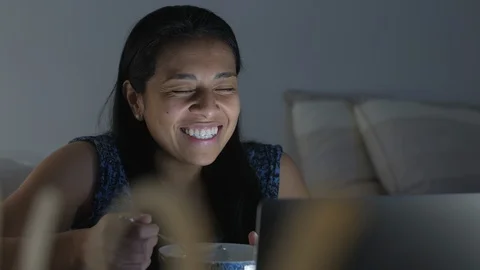 A hispanic girl is sitting in bed in front of a laptop, eating and talking Vídeo Stock 128391153