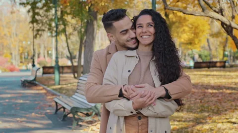 Hispanic guy hugs tight beloved girlfriend from behind in autumn park happy 스톡 동영상 165881617